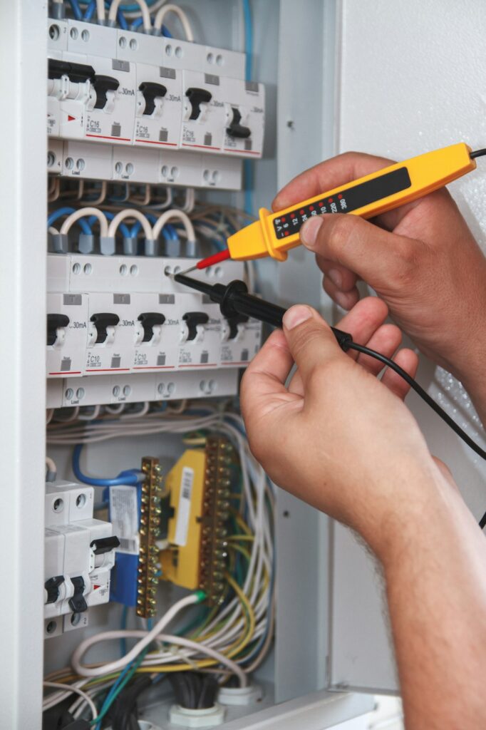 Electrician with multimeter probe at an electrical switchgear ca